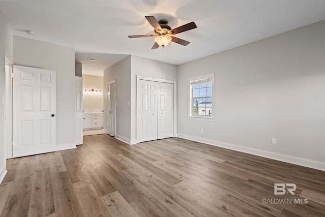 unfurnished bedroom featuring baseboards, connected bathroom, ceiling fan, wood finished floors, and a closet