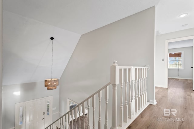 hall featuring baseboards, vaulted ceiling, wood finished floors, and an upstairs landing