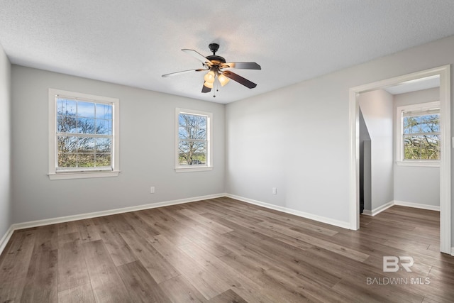 unfurnished room with a textured ceiling, wood finished floors, a wealth of natural light, and baseboards