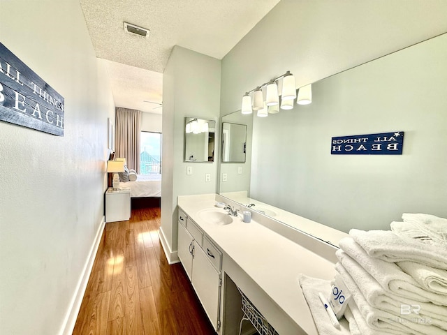 ensuite bathroom with wood finished floors, ensuite bath, baseboards, visible vents, and a textured ceiling