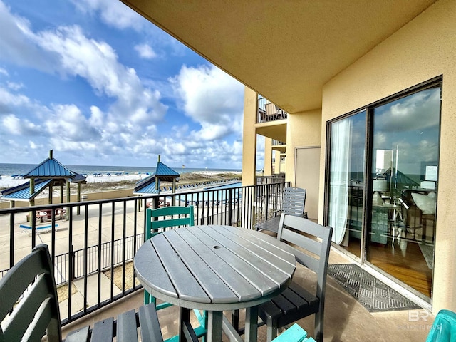 balcony with a beach view, outdoor dining area, and a water view