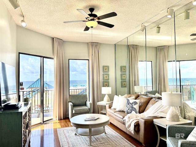 living room with a textured ceiling, wood finished floors, a ceiling fan, and a water view