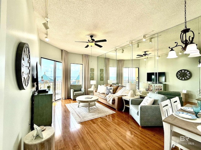 living area with track lighting, wood finished floors, a ceiling fan, and a textured ceiling