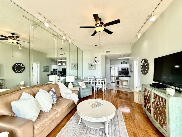 living room featuring rail lighting, wood finished floors, a ceiling fan, and visible vents
