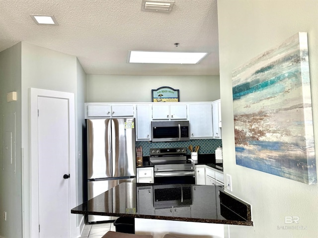 kitchen featuring visible vents, stainless steel appliances, white cabinets, and backsplash