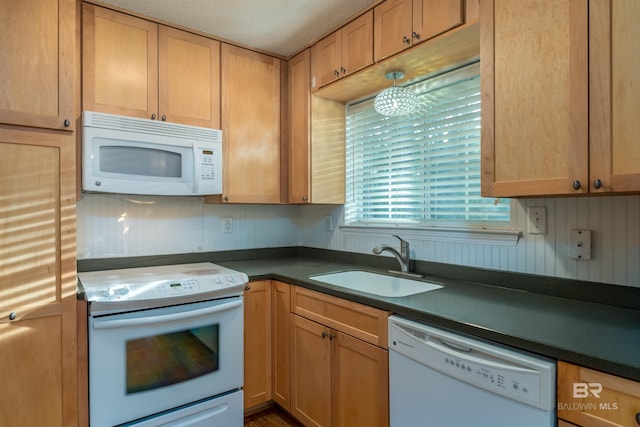 kitchen with white appliances, dark countertops, and a sink