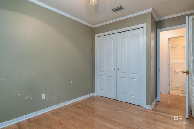 unfurnished bedroom featuring baseboards, visible vents, crown molding, light wood-style floors, and a closet