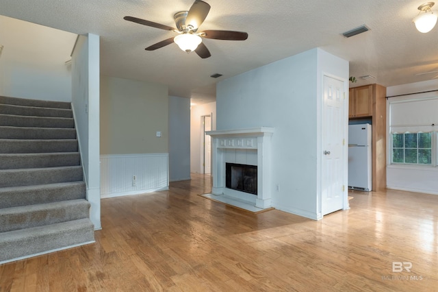 unfurnished living room featuring light wood finished floors, stairs, a textured ceiling, and a tile fireplace