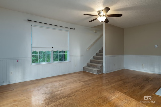 spare room featuring a wainscoted wall, wood finished floors, a textured ceiling, and stairs