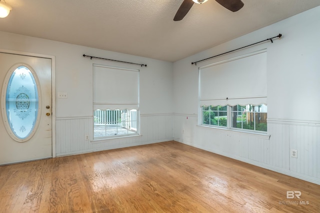 foyer entrance with a textured ceiling, wainscoting, wood finished floors, and a ceiling fan