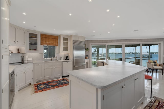 kitchen with a large island, white cabinets, backsplash, a water view, and built in refrigerator