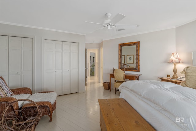 bedroom featuring ceiling fan, crown molding, light hardwood / wood-style flooring, and two closets