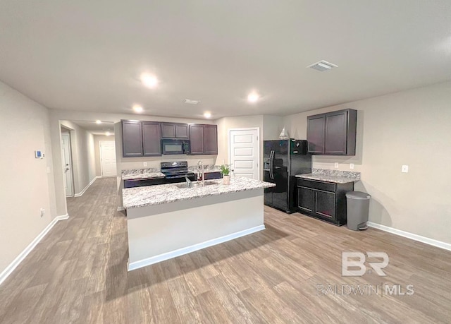 kitchen with an island with sink, sink, dark brown cabinetry, black appliances, and light hardwood / wood-style flooring