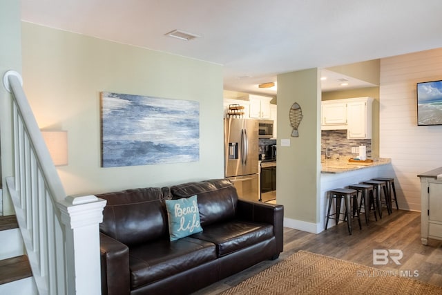 living room featuring stairs, visible vents, baseboards, and wood finished floors