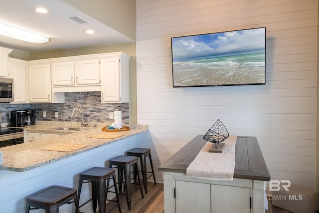 kitchen with visible vents, light stone counters, stainless steel microwave, a kitchen bar, and a sink