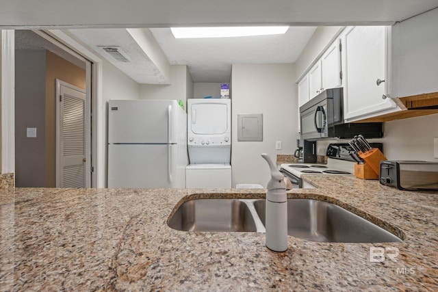 kitchen featuring white cabinets, white fridge, a textured ceiling, stacked washer and dryer, and electric range