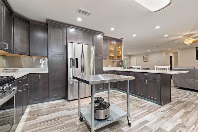 kitchen with appliances with stainless steel finishes, ceiling fan, dark brown cabinets, light hardwood / wood-style flooring, and kitchen peninsula