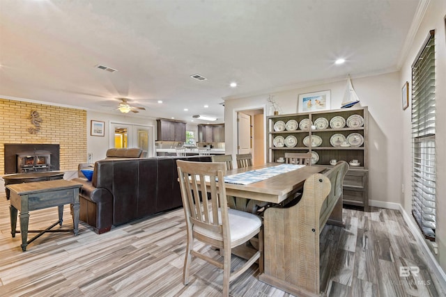 dining space with ceiling fan, a brick fireplace, brick wall, crown molding, and light hardwood / wood-style flooring