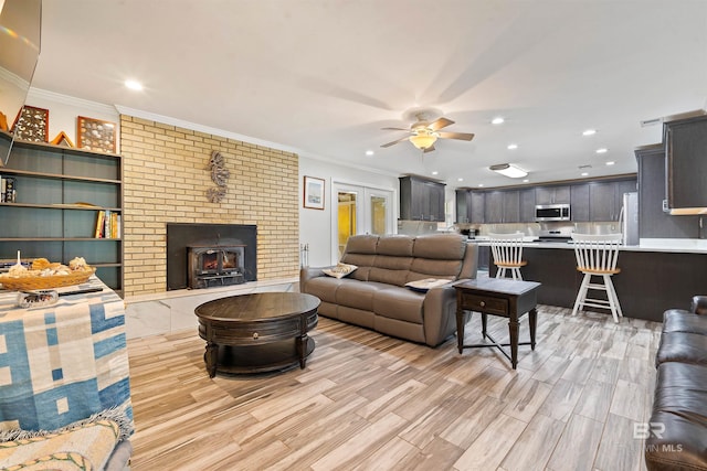 living room with ceiling fan, crown molding, light wood-type flooring, and a fireplace