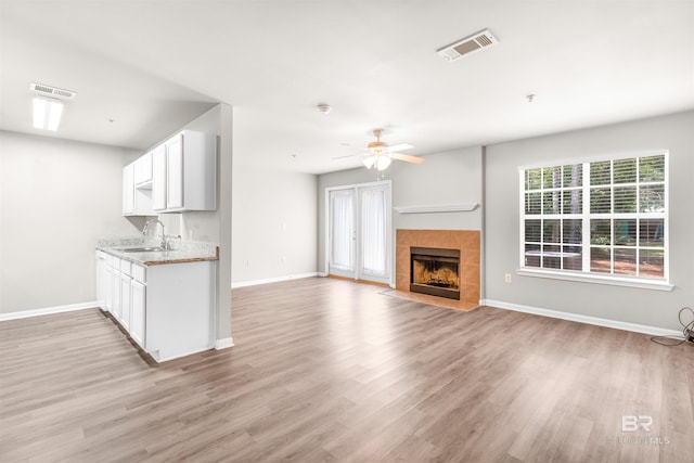 unfurnished living room with sink, light hardwood / wood-style floors, a tile fireplace, and ceiling fan