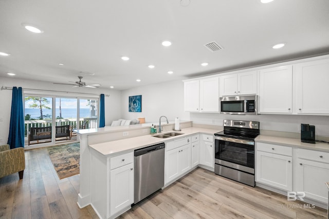 kitchen with visible vents, appliances with stainless steel finishes, open floor plan, a sink, and a peninsula