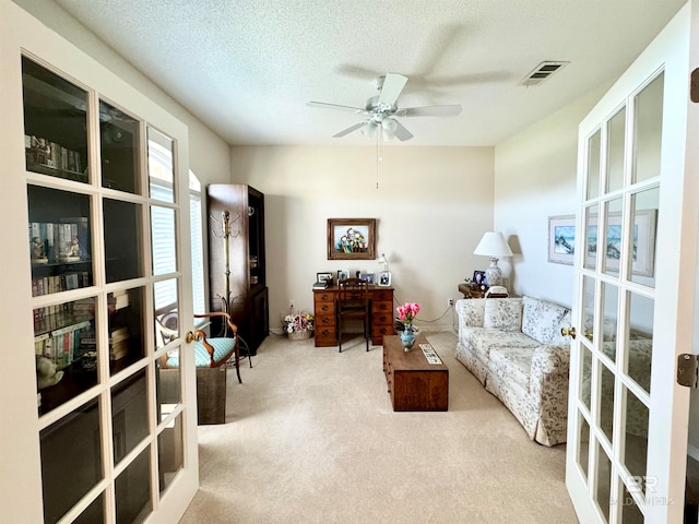 interior space featuring ceiling fan, light colored carpet, french doors, and a textured ceiling