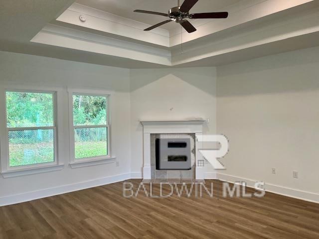 unfurnished living room with ceiling fan, hardwood / wood-style floors, a tiled fireplace, and a tray ceiling