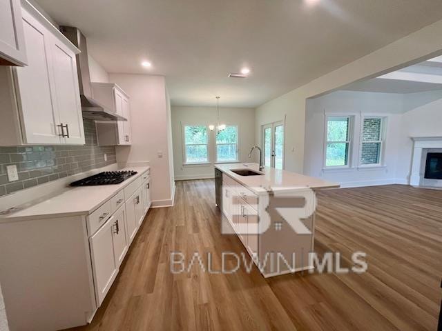 kitchen featuring white cabinets, black appliances, hanging light fixtures, light wood-type flooring, and sink