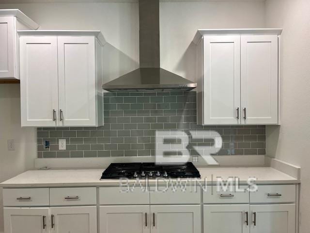 kitchen with wall chimney range hood, decorative backsplash, and white cabinetry