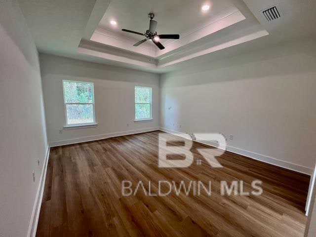 unfurnished room featuring wood-type flooring, ceiling fan, and a tray ceiling