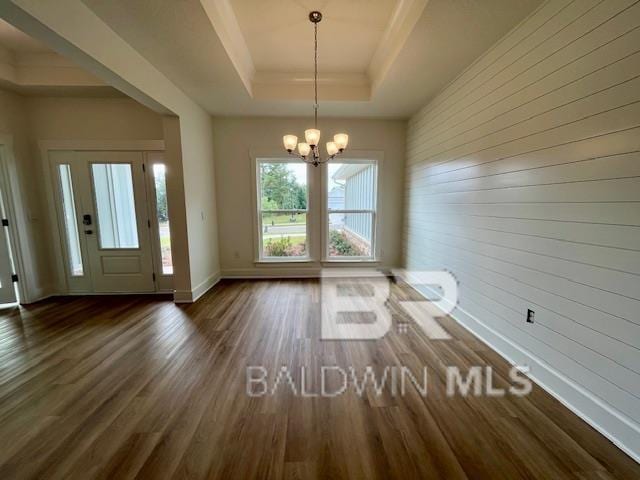 interior space with dark wood-type flooring, an inviting chandelier, a tray ceiling, and wooden walls