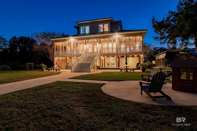 back house at twilight with a porch, a patio, and a lawn