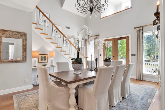 dining space with french doors, a high ceiling, a notable chandelier, crown molding, and light hardwood / wood-style floors