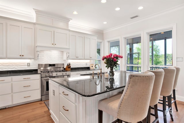 kitchen featuring white cabinetry, high end stainless steel range oven, light hardwood / wood-style floors, a kitchen island with sink, and ornamental molding