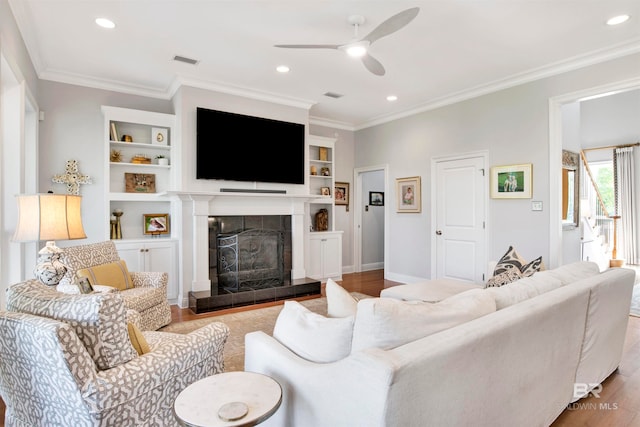 living room with ceiling fan, crown molding, a tile fireplace, hardwood / wood-style flooring, and built in features