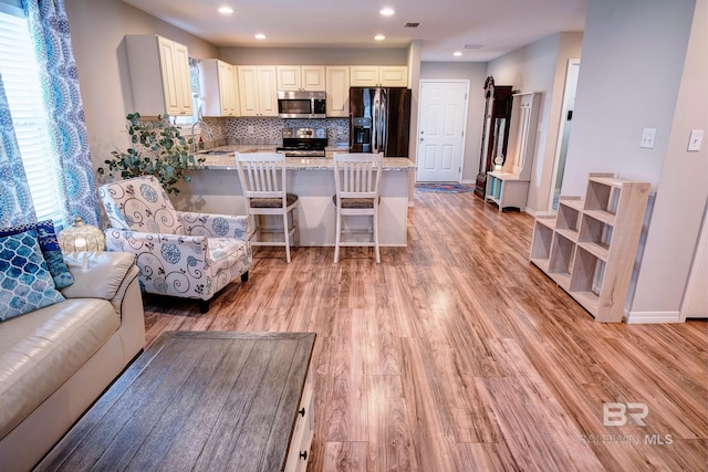 kitchen featuring light stone countertops, tasteful backsplash, appliances with stainless steel finishes, a peninsula, and light wood-style floors