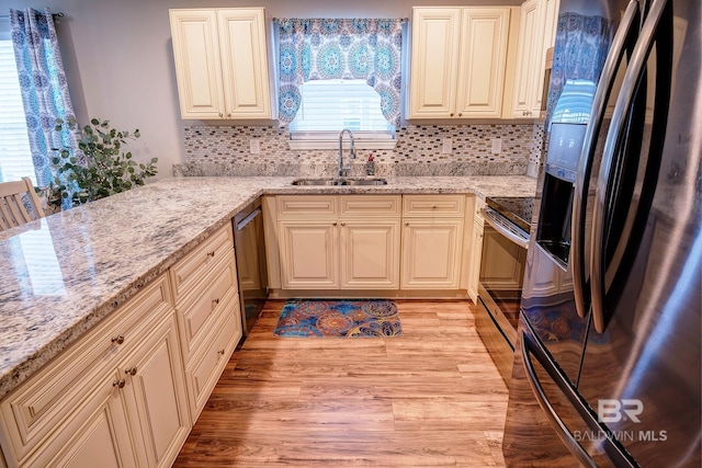 kitchen featuring backsplash, a sink, light stone countertops, stainless steel appliances, and light wood-style floors