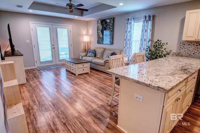 living area with french doors, a ceiling fan, a raised ceiling, light wood-type flooring, and visible vents