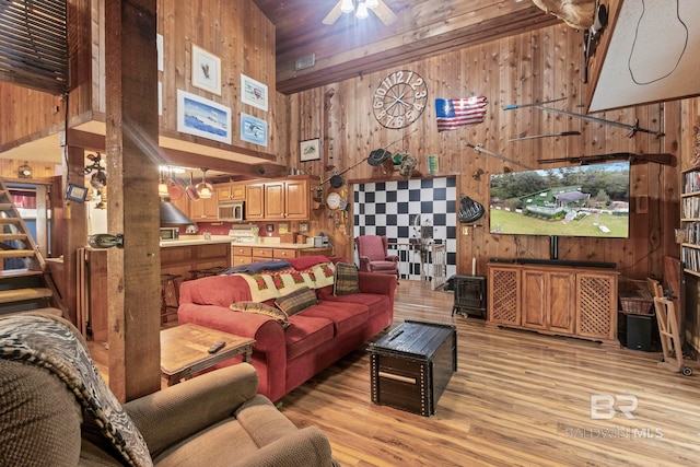 living room with a high ceiling, light hardwood / wood-style floors, ceiling fan, and wood walls