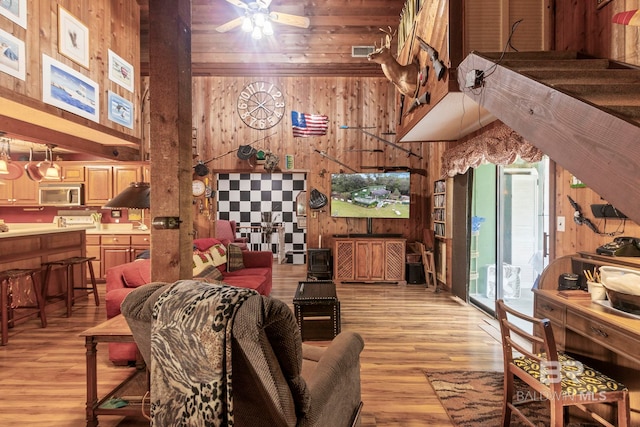 living room with light hardwood / wood-style floors, ceiling fan, and wooden walls