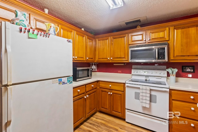 kitchen featuring a textured ceiling, white appliances, and light hardwood / wood-style floors