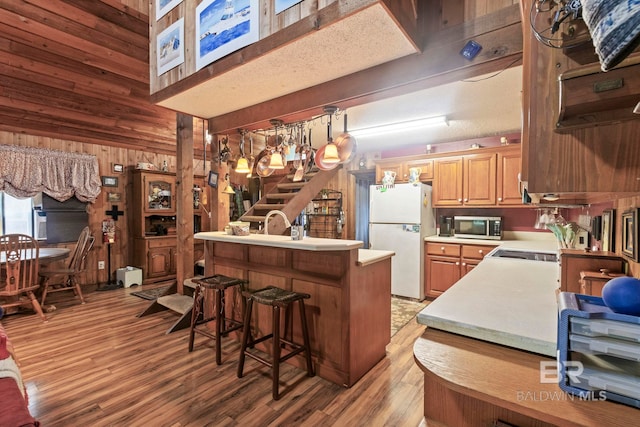 kitchen with a kitchen breakfast bar, white refrigerator, kitchen peninsula, wood walls, and light hardwood / wood-style floors