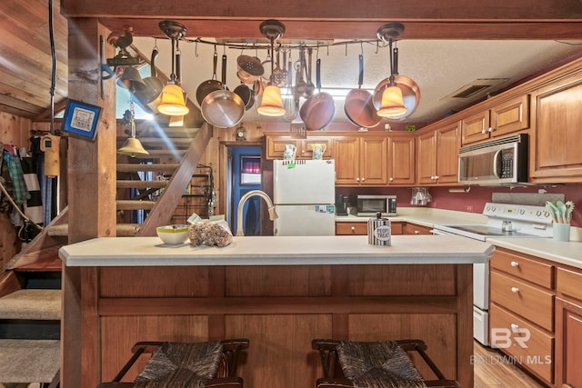 kitchen with sink, a kitchen bar, white appliances, and hanging light fixtures