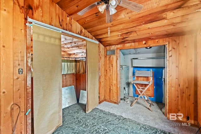 misc room featuring ceiling fan, dark colored carpet, water heater, lofted ceiling, and wooden walls