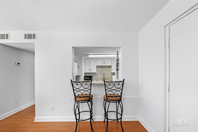 kitchen with backsplash, light hardwood / wood-style flooring, a textured ceiling, a kitchen bar, and white cabinetry