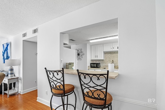 kitchen with white cabinetry, kitchen peninsula, light hardwood / wood-style floors, a breakfast bar area, and decorative backsplash