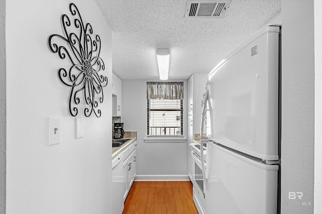 kitchen with white cabinetry, white refrigerator, light wood-type flooring, a textured ceiling, and range