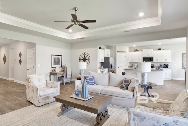 11569 Thistledown Loop, Spanish Fort, AL 36527 - living room with a raised ceiling, light wood-type flooring, baseboards, crown molding, and a ceiling fan