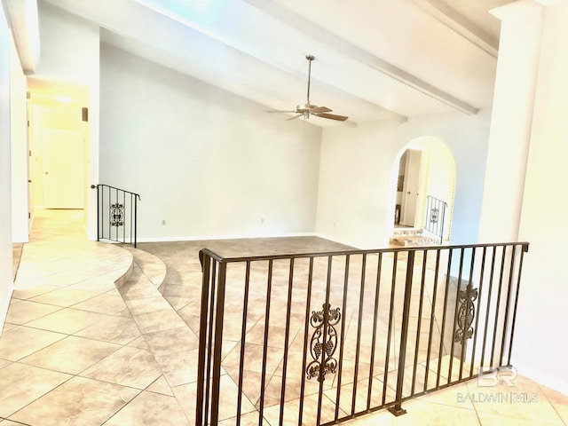 tiled spare room with baseboards, beam ceiling, arched walkways, and a ceiling fan