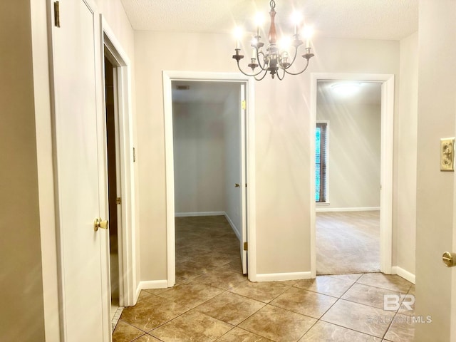 corridor featuring light tile patterned floors, baseboards, a textured ceiling, and an inviting chandelier